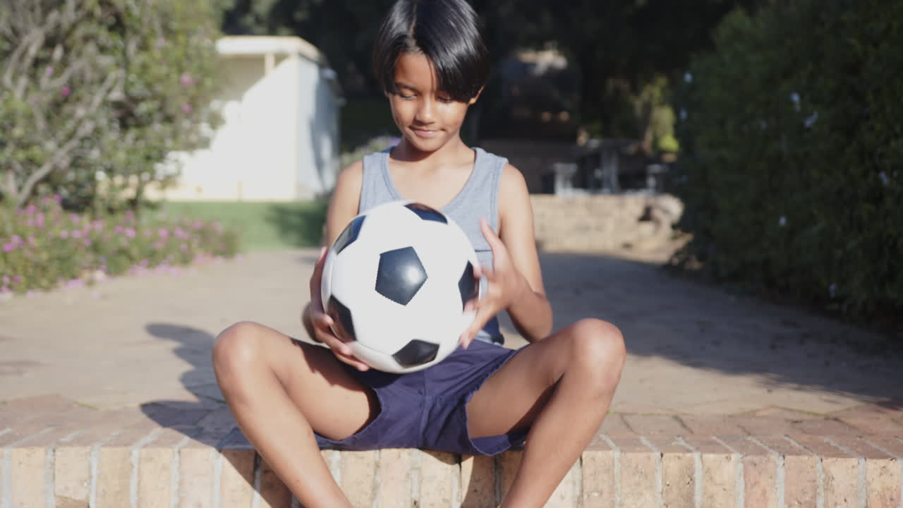 Sitting outdoors, boy holding soccer ball and smiling, enjoying break from school