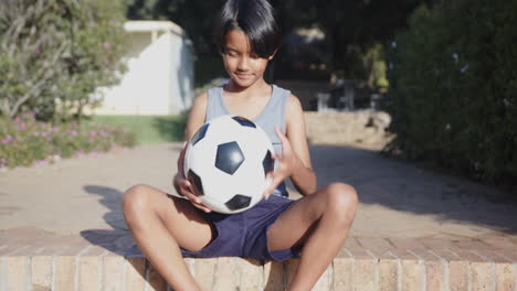 sitting outdoors, boy holding soccer ball and smiling, enjoying break from school