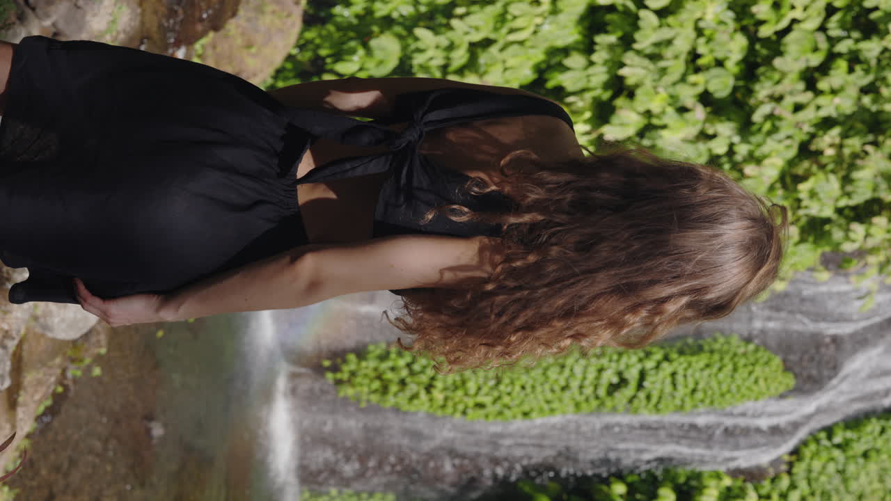 Femme se tenant près d'une cascade avec un arc-en-ciel dans la brume
