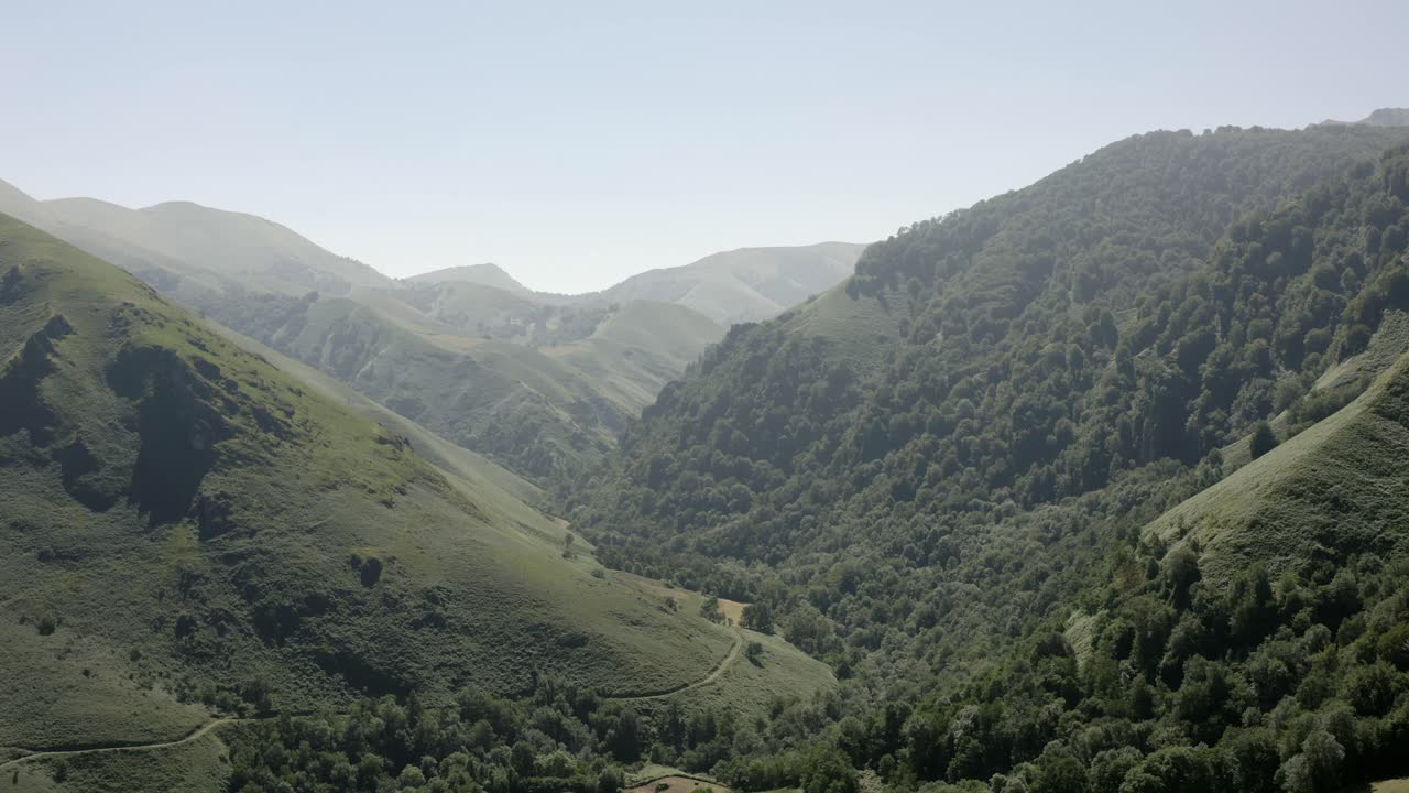 Flyover grassy mountain valley slopes in French Pyrenees, small road