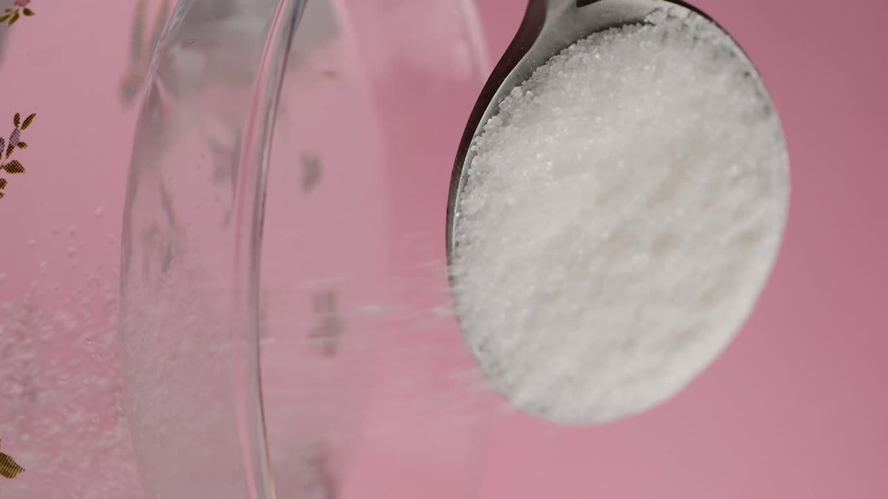 Pouring sugar into a glass with a spoon