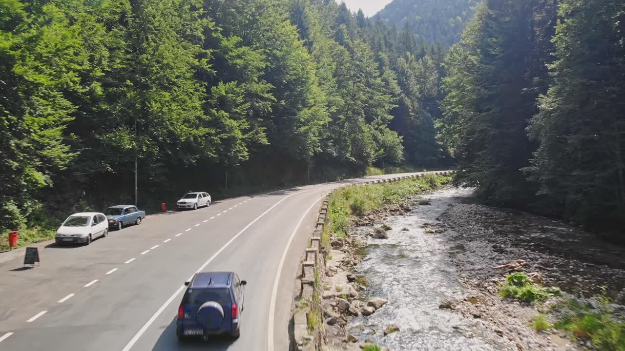Blue car driving on the road in the mountains near the forest. Firs at the edge of the road. Aerial drone shot