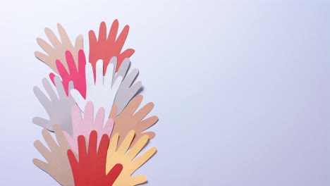 close up of hands together made of colourful paper on blue background with copy space