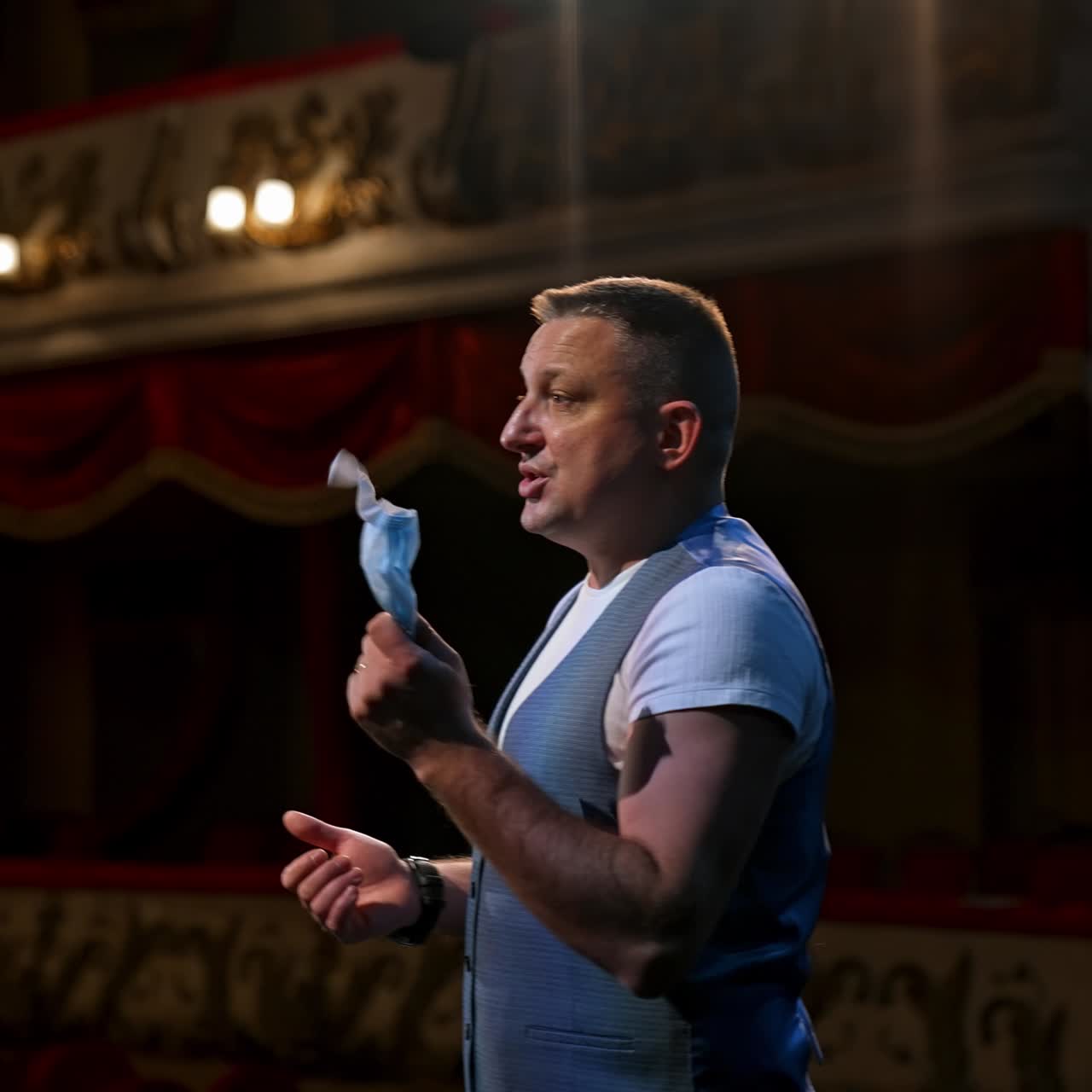 Man with medical mask in hands standing on stage and speaks seriously. Rehearsal during covid-19