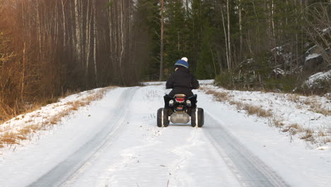 un niño pequeño conduce una bicicleta cuádruple en una carretera desierta en un bosque frío de invierno en el norte de finlandia