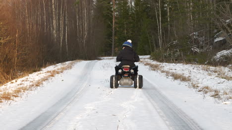 little kid drives quad bike on deserted road in cold winter forest in northern finland