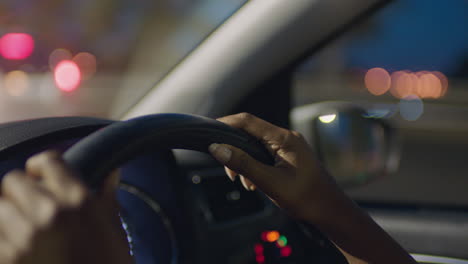 woman driving car with hands on steering wheel in city at night travelling on the road to destination