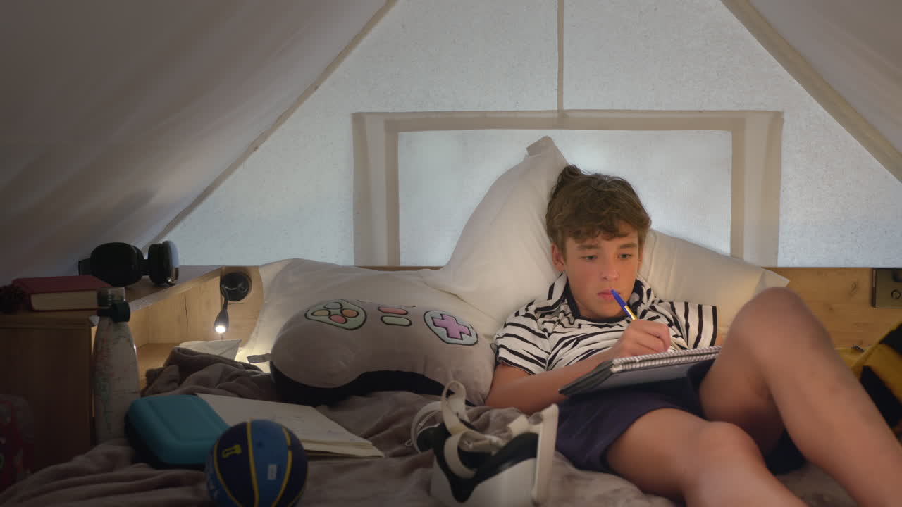 십대 소년 이 편안 한 텐트 침대 에서 숙제를 하고 있다