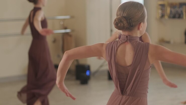 Un gruppo di giovani allievi di danza classica in abbigliamento da ballo nero che eseguono esercizi in un ampio studio di danza con pavimenti in legno e barre a muro. Espressioni concentrate e movimenti sincronizzati