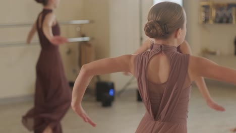 a group of young ballet students in black dancewear practicing positions in a spacious ballet studio with wooden flooring and wall-mounted barres. focused expressions and synchronized movements.