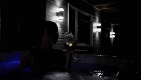 weibliches porträt im dunkeln, das sich im jacuzzi entspannt und nachts wein trinkt