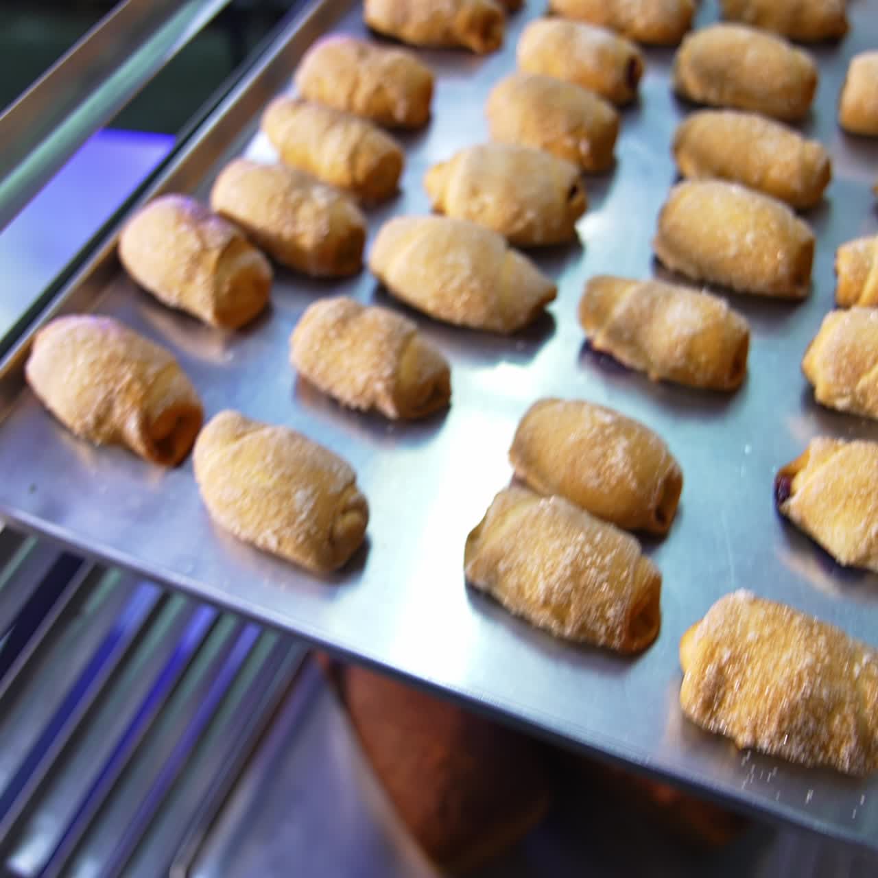 Metal baking sheet filled with freshly baked little croissants. Close up. Sweet desserts production at modern bakery