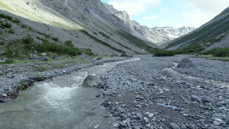 aerial drone footage flying low and close to a fast flowing river in a glacial valley surrounded by a steep and dramatic mountain landscape with residual patches of snow in switzerland