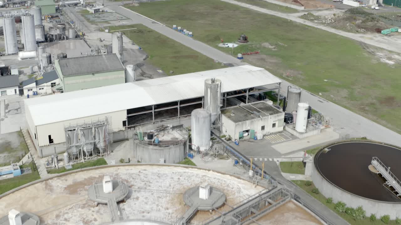 Aerial forward reveal over DRT large industrial factory site, including storage buildings and circular water treatment tanks, Veille-Saint-Girons, France