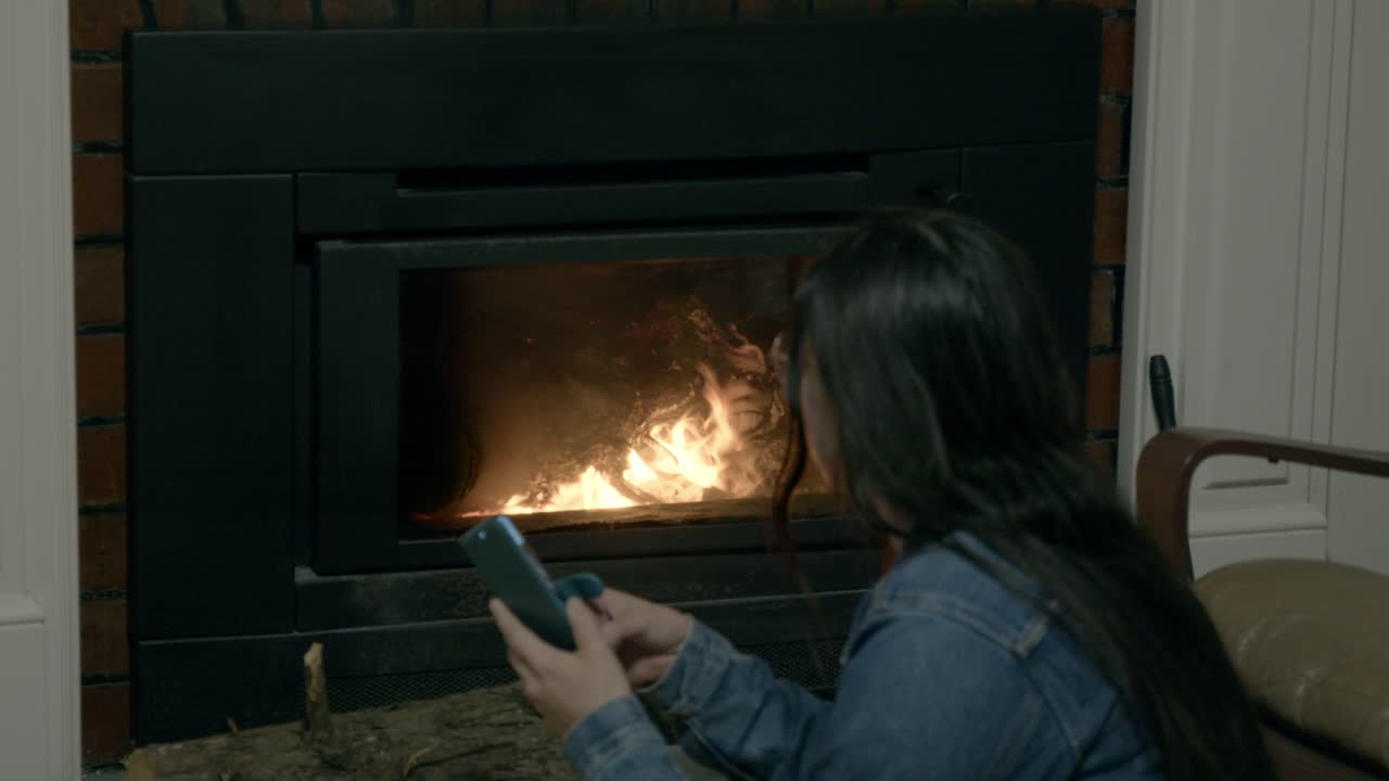 A young girl in a denim jacket, tending to a warm fire indoors with logs nearby. The soft glow of the flames creates a soothing, intimate atmosphere perfect for relaxation