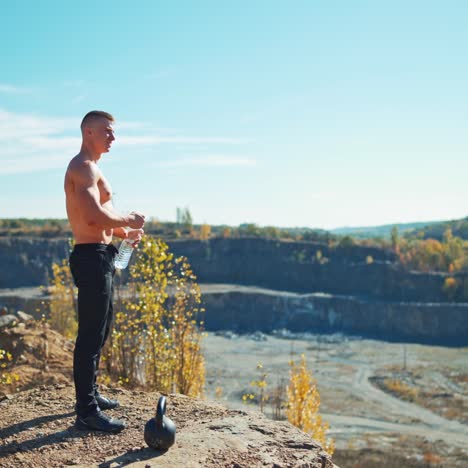 side view of a sportsman drinks water after workout. young athlete standing on the rocky hill and drinking water from a bottle in summer.