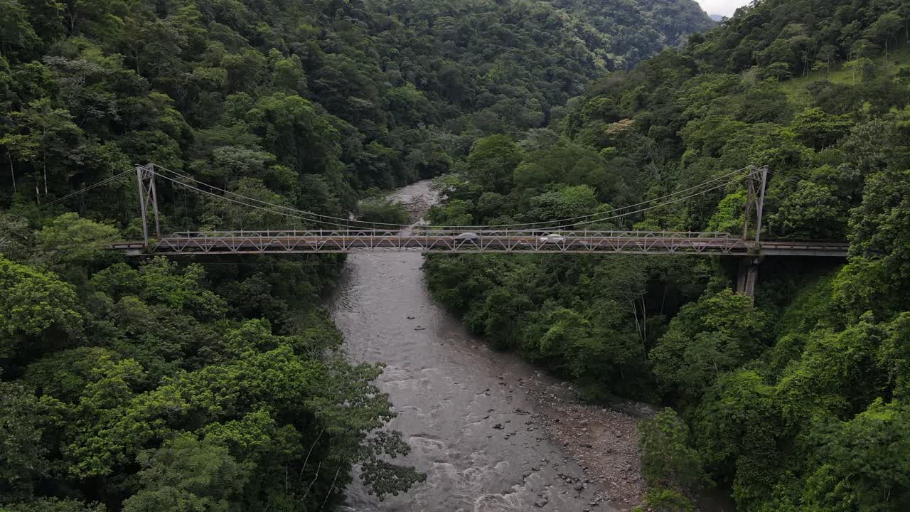 4k cinematic aerial footage of Puente Río Peñas Blancas. Old Steel bridge in the middle of the jungle in Costa Rica. Several cars crossing the ancient construct while drone is slowly ascending