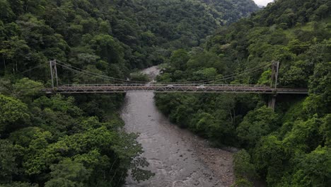 4k cinematic aerial footage of puente río peñas blancas. old steel bridge in the middle of the jungle in costa rica. several cars crossing the ancient construct while drone is slowly ascending