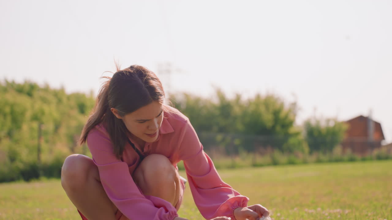 Young Girl Gently Pets Playful Puppy, Female Gently Caresses Energetic Puppy Lying On Grass In Sunlight, Woman Tenderly Plays With Joyful Young Dog Resting On Lush Green Grass Under Bright Sunshine