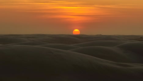 Hermosa-Toma-Aérea-Cinematográfica-De-Un-Gran-Sol-Naranja-Poniéndose-Sobre-Las-Dunas