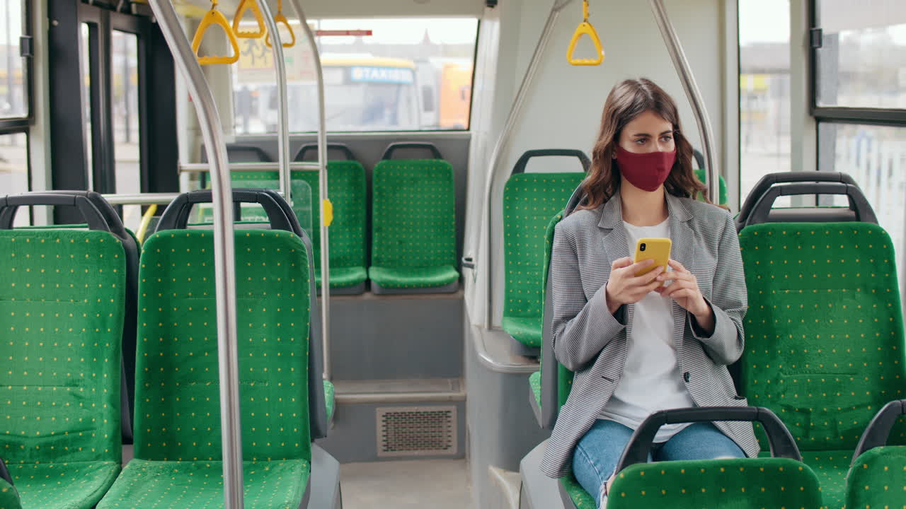 Young woman wearing a face mask using a smartphone on an empty public bus