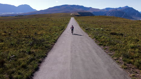 cyclist on straight mountain road between fynbos vegetation, hermanus