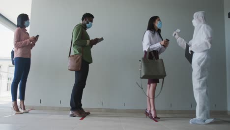 health worker wearing protective clothes measuring temperature of people standing in a queue