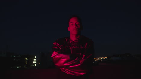 portrait mixed race man with arms crossed posing in city at night looking confident with red light