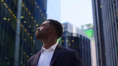 retrato de un joven empresario confiado que lleva un traje de pie afuera mirando hacia las oficinas en el distrito financiero de la ciudad de londres, reino unido.