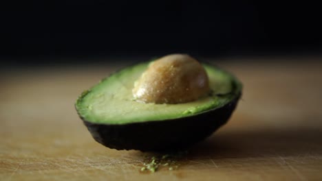 Half-of-green-avocado-with-pit-rotating-on-wooden-chopping-board,-SLOW-MOTION