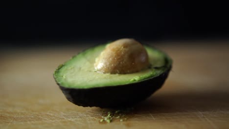 half of green avocado with pit rotating on wooden chopping board, slow motion