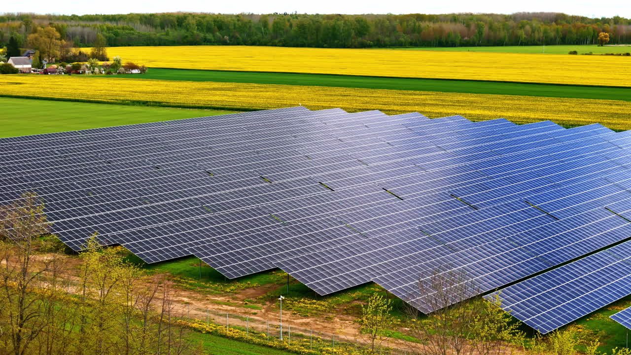 Solar Power Plant Lying On Green Fields Overlooking Rapeseed Fields. Aerial Drone Shot