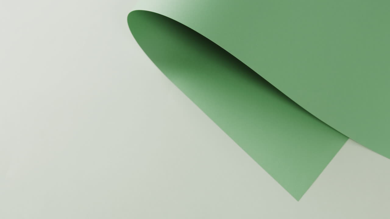 Close up of green rolled piece of paper on white background with copy space in slow motion