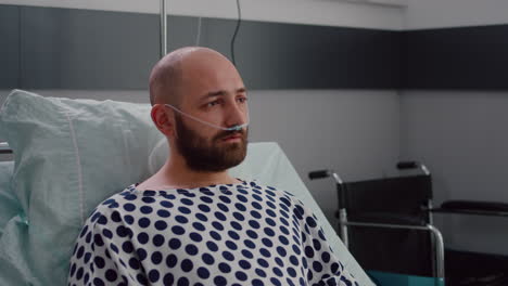 sad sick man with nasal oxygen tube resting in bad looking into camera