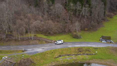 Aerial-tracking-a-camper-van-parking-on-a-road-next-to-a-lake-in-the-Alps,-Switzerland