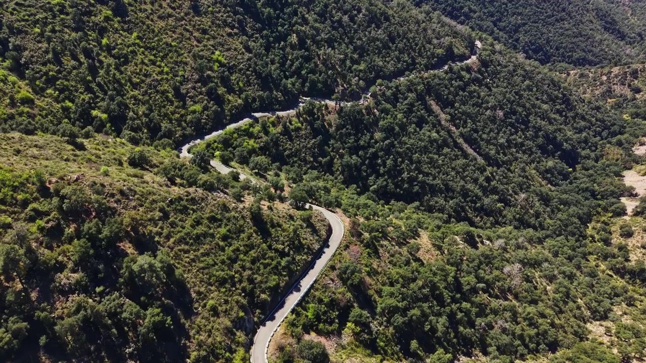 Carretera serpenteante que atraviesa colinas verdes en una zona montañosa durante el día.