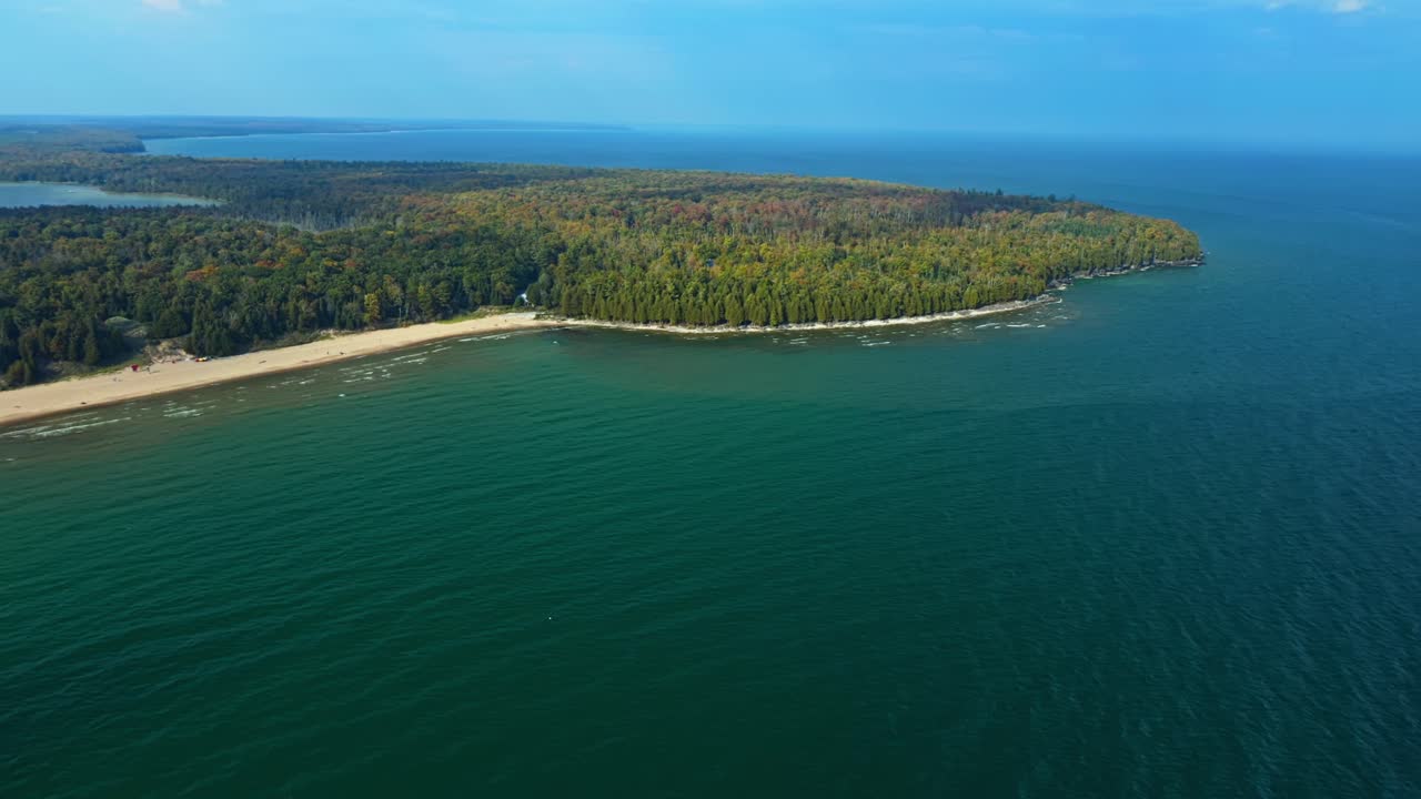 The sweeping curve of sand and forest stretches into Lake Michigan’s shimmering blue, where Door County’s wooded peninsula meets the calm horizon under soft afternoon light
