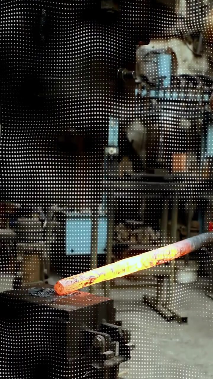 Vertical video: Male metalworker lowering glowing bar onto anvil through mesh screen, forging metal