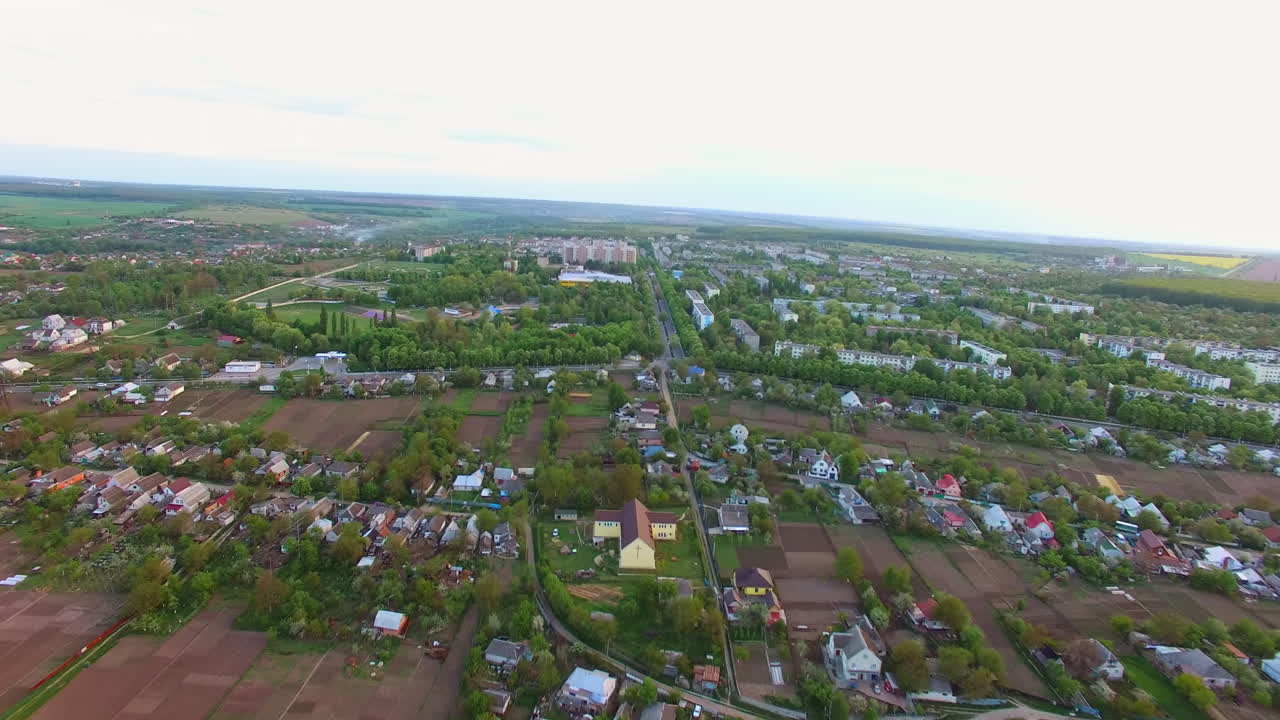 Peaceful little town panorama at daytime. Private houses neighboring farmlands and blocks of flats in the green area.