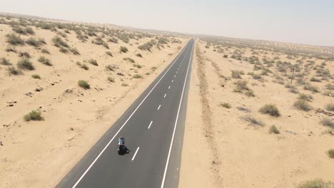 Aerial drone shot flying above a motorbike moving steadily through the sun-soaked desert roads.