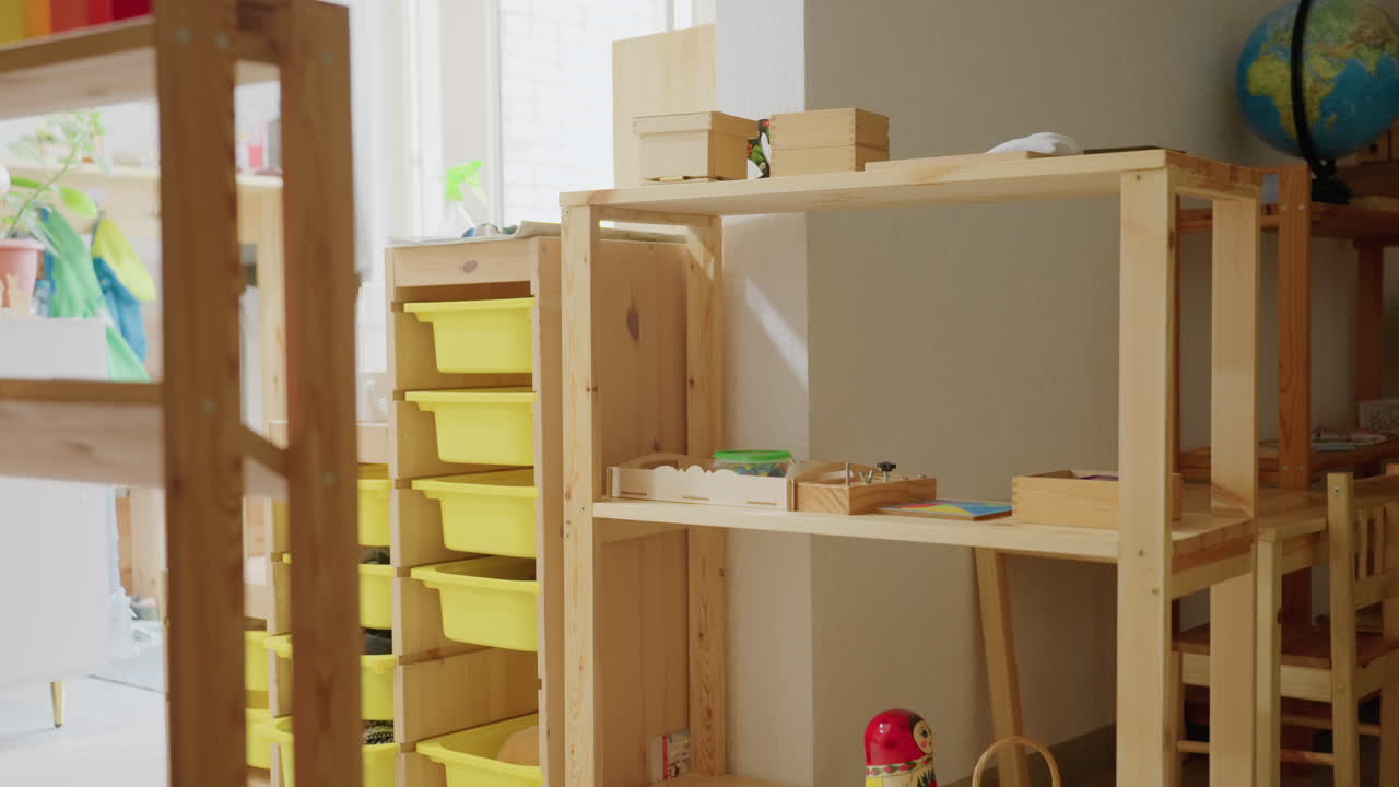 Bright Montessori kindergarten room featuring neatly arranged wooden shelves with boxes, globe, and educational tools near window under daylight, representing early learning environment