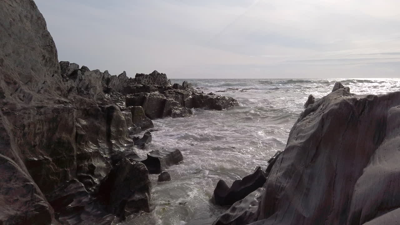 슬로우 모션으로 일몰 시 바위 해변의 좁은 틈에 부서지는 파도