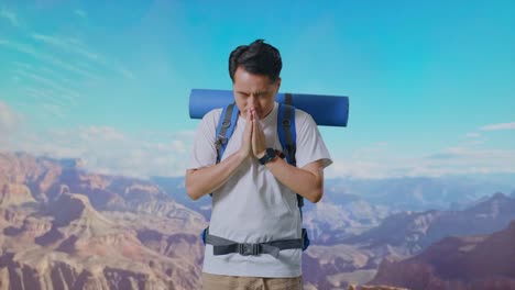 asian male hiker with mountaineering backpack pray for something while traveling at the top of mountain