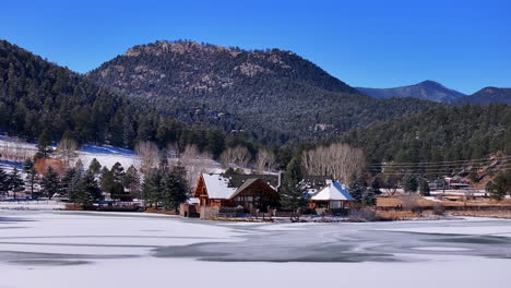 Primera-Nieve-Hielo-Congelado-Cubierto-Blanco-Hoja-Perenne-Lago-Casa-Montaña-Rocosa-Paisaje-Escena-Mañana-Frente-Rango-Denver-Antena-Cinematográfico-Zumbido-Navidad-Patinaje-Sobre-Hielo-Hockey-Cielo-Azul-Círculo-Izquierda-Movimiento