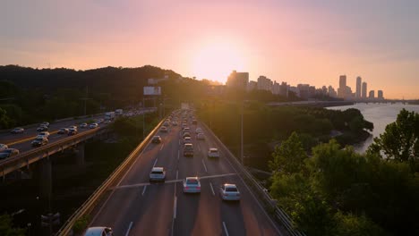 Puesta-De-Sol-Colorida-En-Seúl-Sobre-El-Tráfico-De-La-Autopista-Olímpica-Por-El-Río-Han-Y-La-Silueta-De-Los-Rascacielos-Yeouido---Vista-Aérea-Del-Día-De-Verano,-República-De-Corea