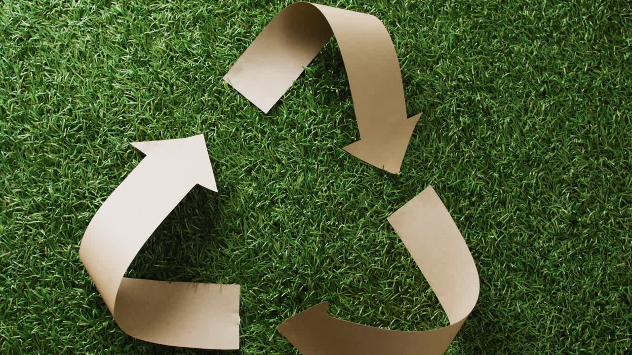 primer plano del símbolo de reciclaje de flechas de papel sobre fondo de hierba, con espacio para copiar