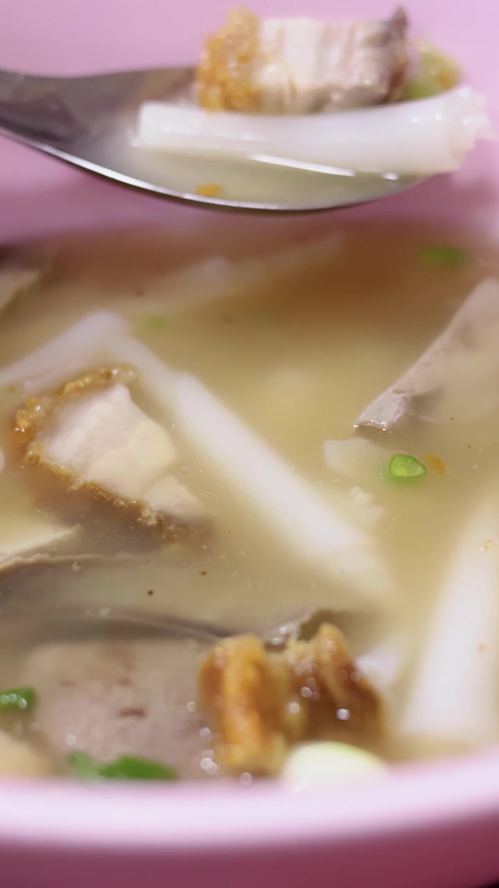 Nærbillede af en ske, der løfter rullede risnudler og sprødt svinekød fra en gadekøkken-suppe skål.