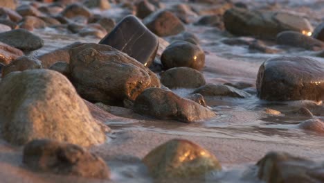 Wellen-Schlagen-An-Einem-Felsigen-Strand-Mit-Weichem,-Warmem-Licht-Mit-Glatten,-Kieselartigen-Felsen