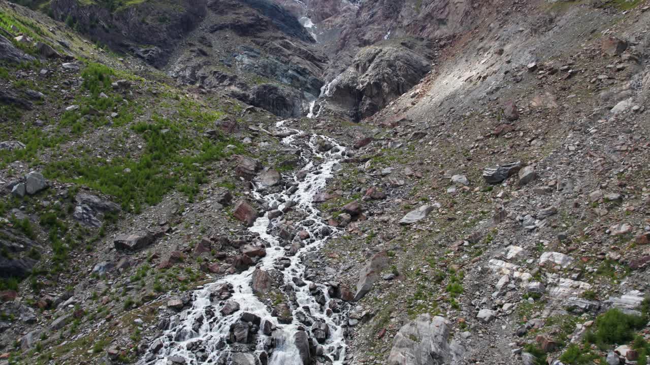 vuelo aéreo sobre una formación montañosa masiva con cascada salvaje y río, impresionante disparo de drones en los alpes suizos en saas-fee