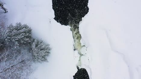 flying over a small water fall on a frozen river during a snow storm slow motion aerial top down